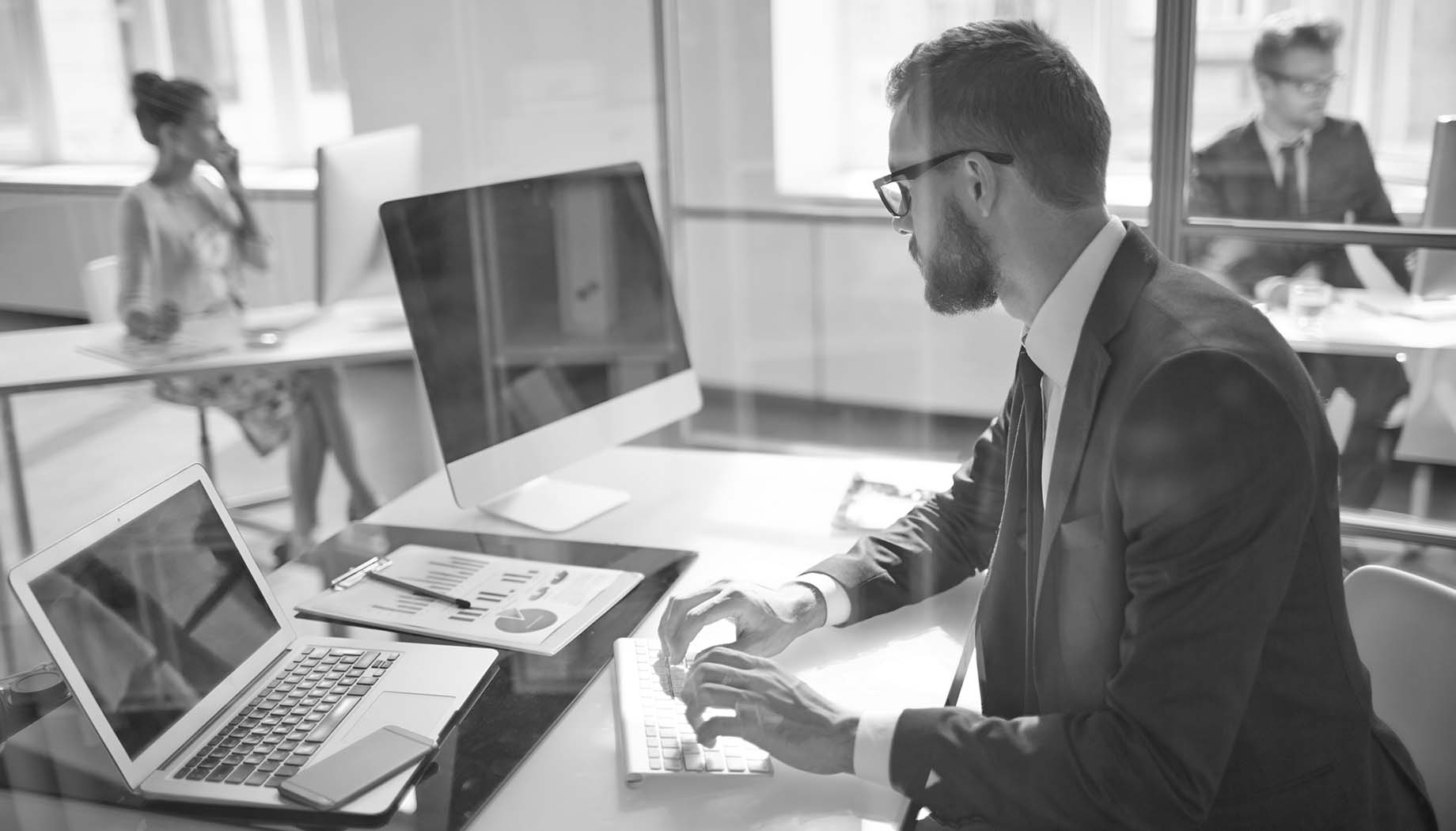 Man in suit sitting at desk typing on apple computer with Macbook and financial charts on his desk