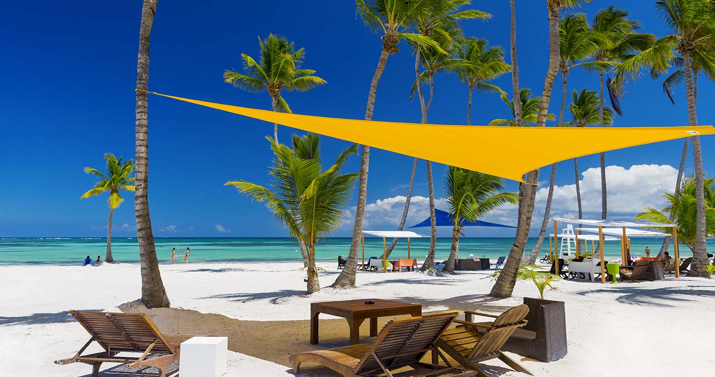 beach with palm tress in the tropics with wooden beach chairs under a shade sail