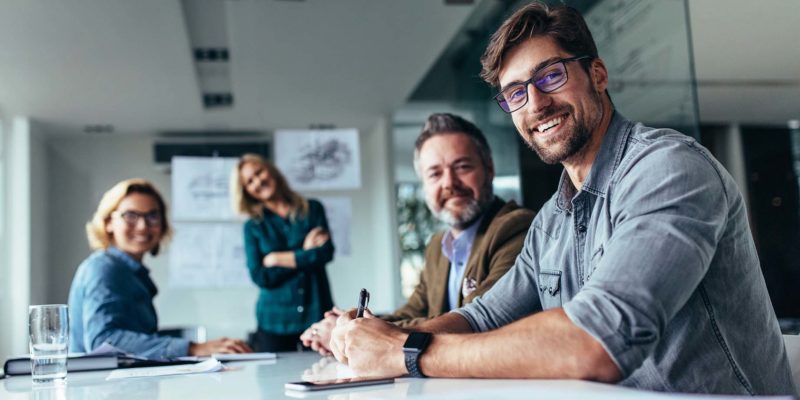 group of men and women working together in office smiling looking at camera